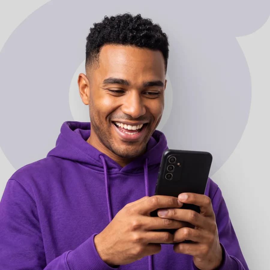 Homem de moletom roxo sorri enquanto usa o celular